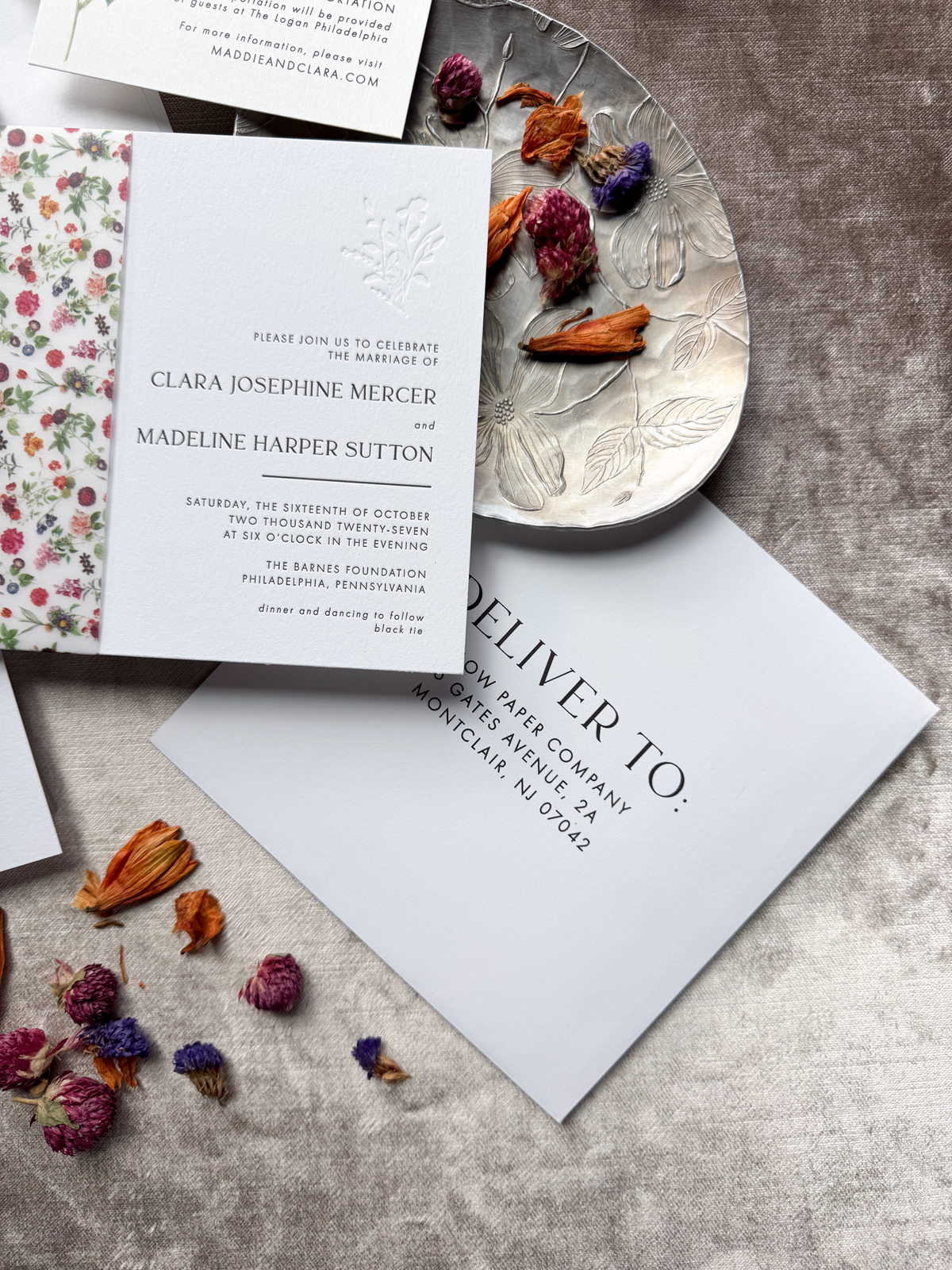 Wedding invitation envelope with floral design on a textured surface with dried flowers.