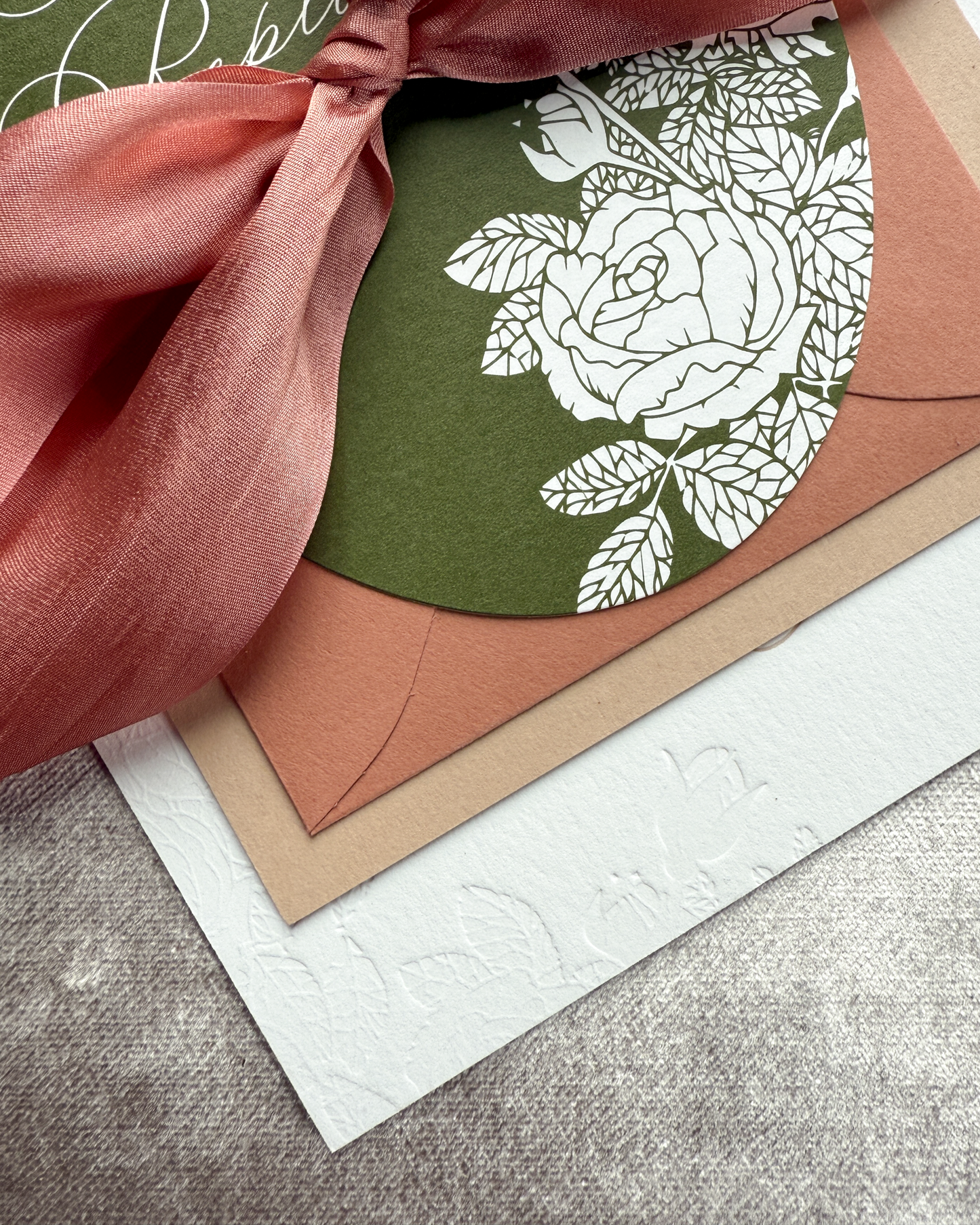 Floral invitation card with terra cotta ribbon on a textured surface