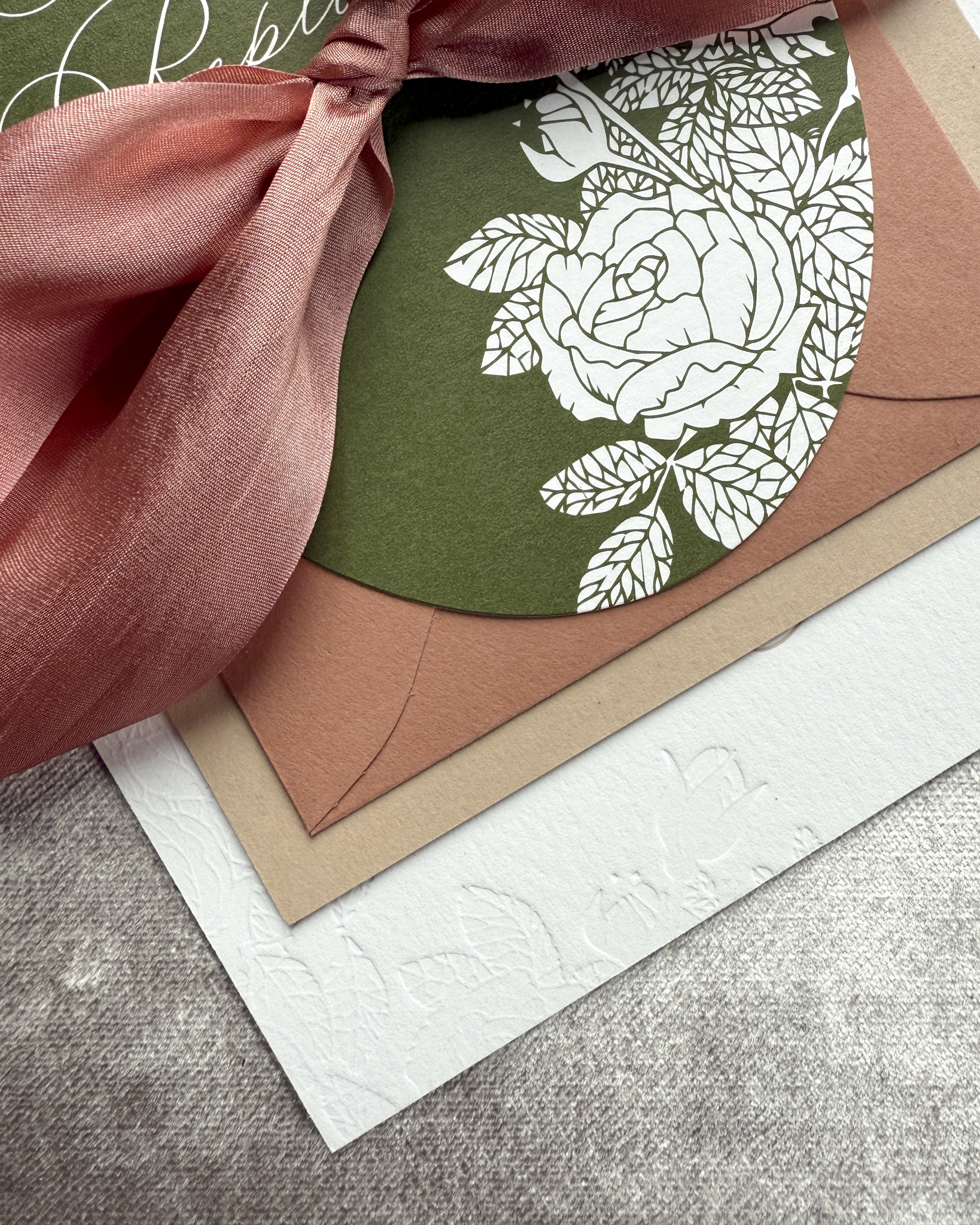 Floral invitation card with terra cotta ribbon on a textured surface