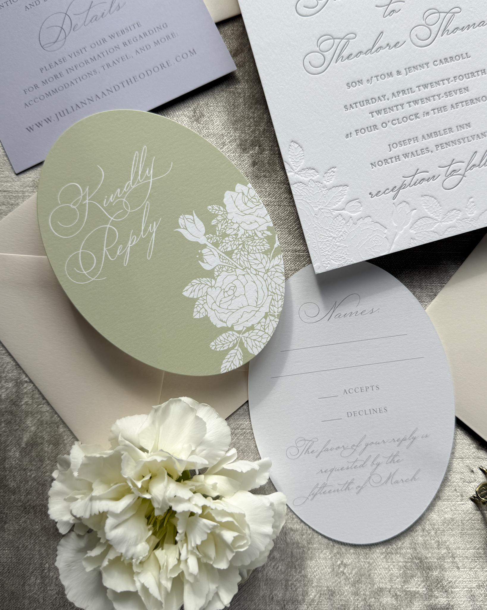 Wedding invitation set with oval die-cut RSVP card and floral design on a textured surface.