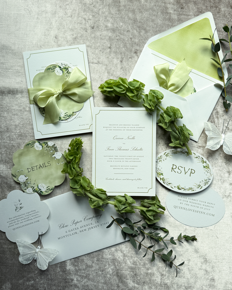 A green wedding invitation suite featuring floral artwork and multiple die-cuts, tied with a green silk ribbon
