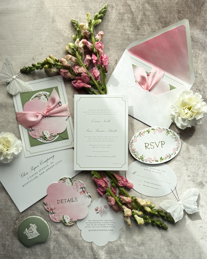 A green and pink wedding invitation suite featuring floral artwork and multiple die-cuts, tied with a pink silk ribbon