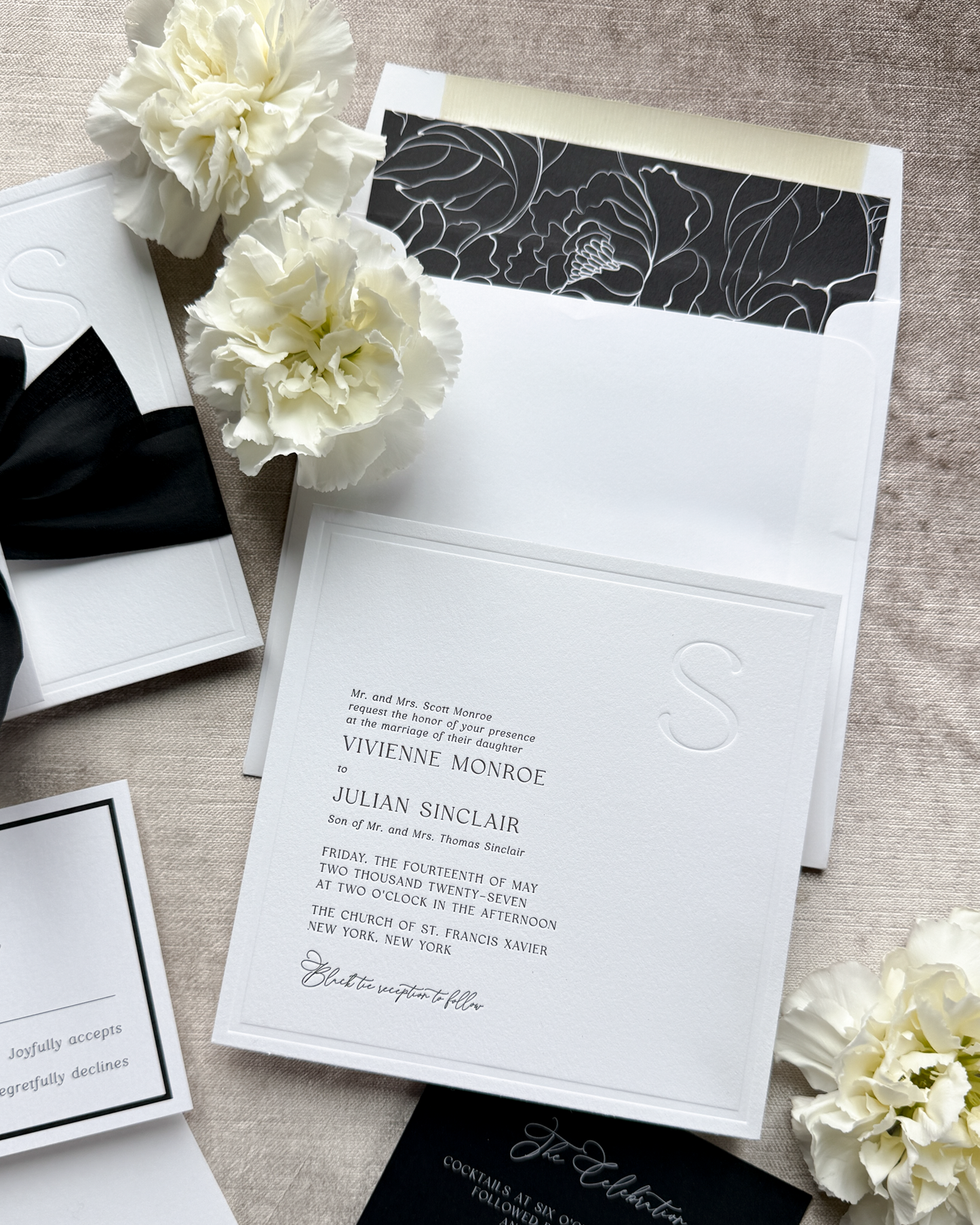 Black and white wedding invitation set with floral decorations on a textured surface