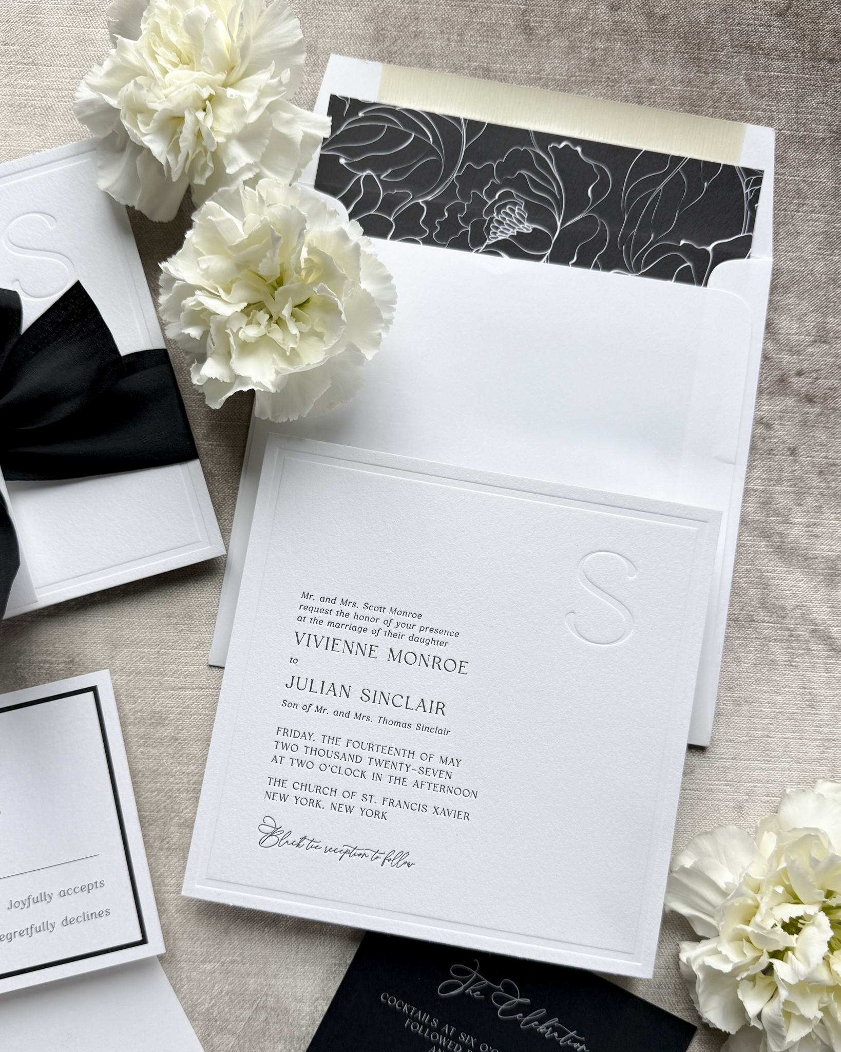 Black and white wedding invitation set with floral decorations on a textured surface