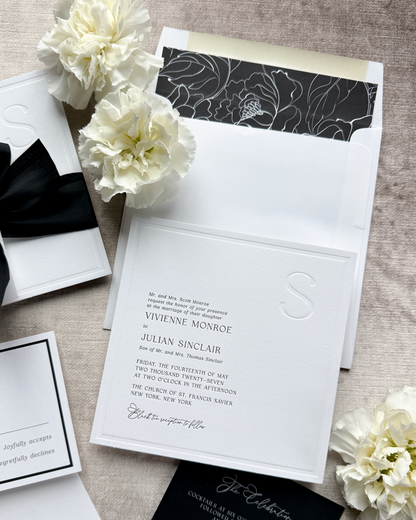 Black and white wedding invitation set with floral decorations on a textured surface