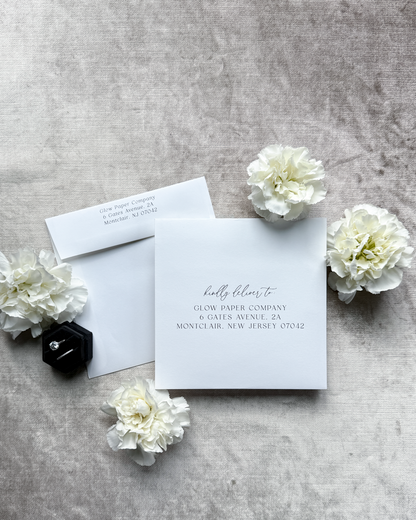Glow Paper Company stationery set with a card and envelope on a gray surface with white flowers.