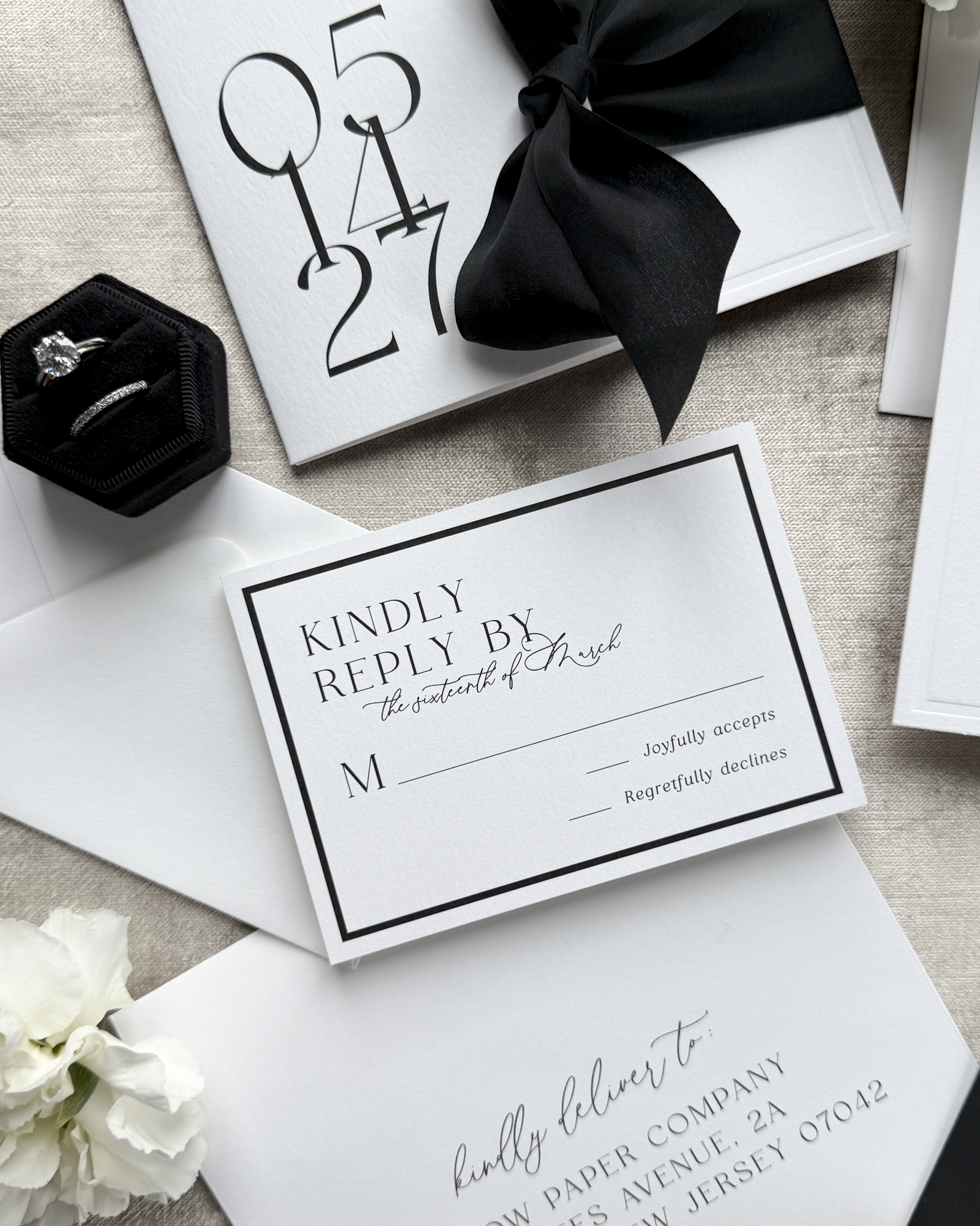 Wedding invitation card with RSVP card and black bow on a textured surface.