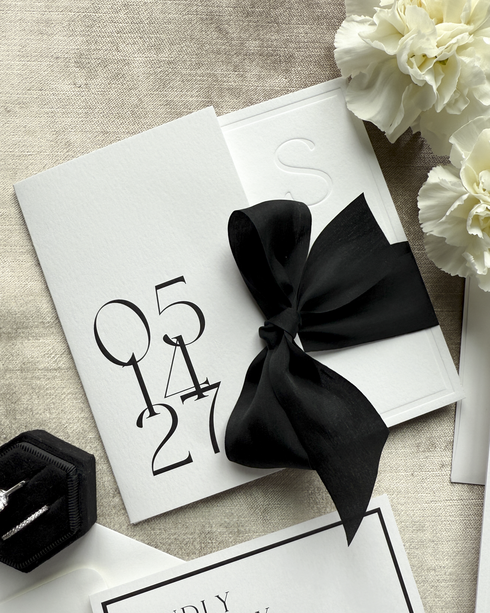 White card with a black bow, surrounded by white flowers on a textured surface.