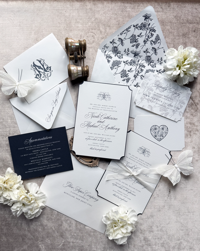 A wedding invitation suite featuring navy text and a vintage floral pattern, tied with a silk ribbon