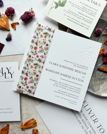 Wedding invitation card with floral design and text on a textured surface with dried flowers.